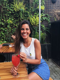 Portrait of a smiling young woman sitting outdoors with a drink