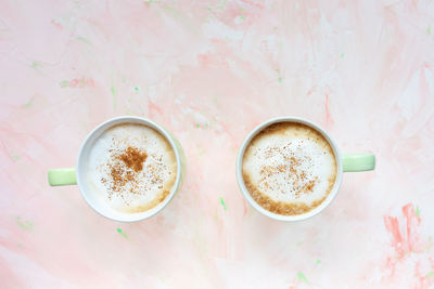 Two cups of latte coffee on light pink background