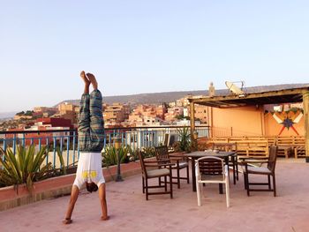 Young man doing handstand on building terrace against clear sky