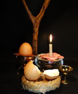 Lit candle with egg against black background during easter