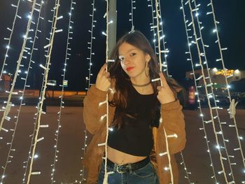 Portrait of young woman standing amidst illuminated decoration at night