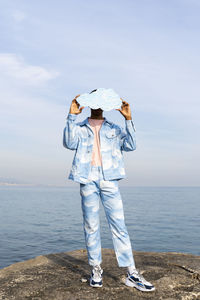 Young man hiding face with cloud cut out while standing against sea
