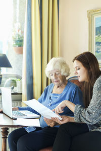 Grandmother and granddaughter reading document while using laptop at home