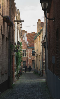 Rear view of people walking on narrow street amidst buildings