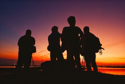 Silhouette men standing at beach against sky during sunset