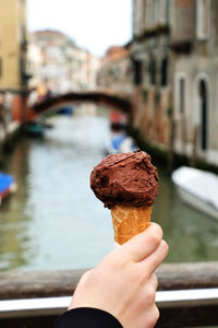 Close-up of hand holding ice cream cone against canal