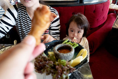 Cropped hand of person showing chicken to cute baby girl sitting in restaurant