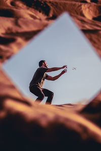 Reflection of man in mirror catching airplane against clear sky