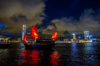 Illuminated city by sea against sky at night