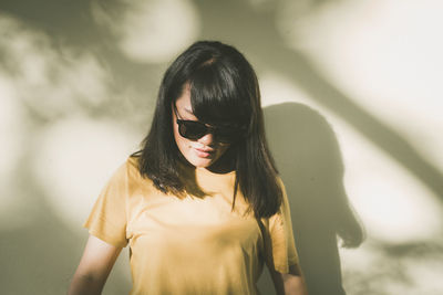 Young woman wearing sunglasses while standing against wall