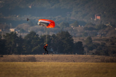 Person paragliding over field against sky