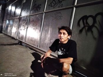 Portrait of young man looking away while sitting on wall