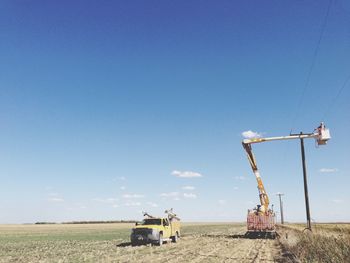 Electric utility worker in truck bucket near pole on landscape