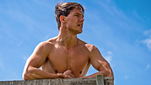 Shirtless man looking away against sky