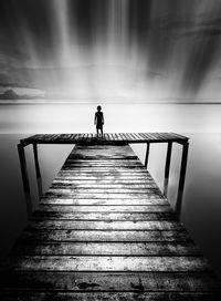 Rear view of boy standing on pier against sea