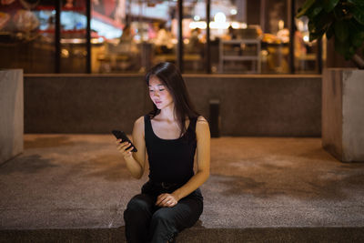 Portrait of young woman using mobile phone while sitting outdoors