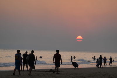 People on beach against sky during sunset