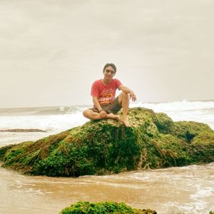 Full length of man sitting on rock at beach