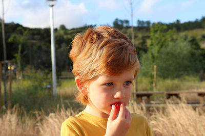 A blond boy eats a cherry and looks into the distance. thoughtful five-year-old boy eats fruits.