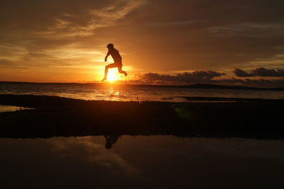 Silhouette man on beach against sky during sunset