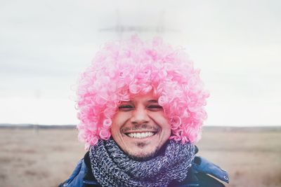 Portrait of smiling young man wearing pink wig against pink sky
