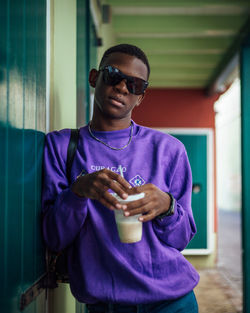 Portrait of man having drink while standing by wall