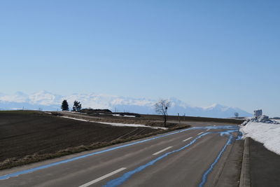 Road leading towards mountains against clear blue sky