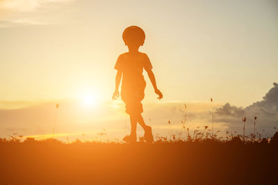 Silhouette boy on field against sky during sunset