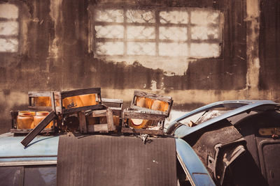 Containers in broken wooden boxes on abandoned car against wall