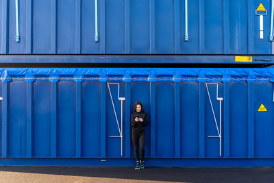 Full length of woman using mobile phone against container