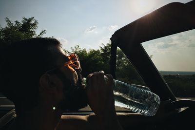 Portrait of man drinking from car against sky