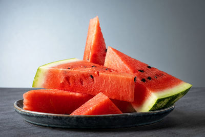 Sliced pieces of ripe sweet watermelon lie on a gray ceramic plate on a gray surface. 