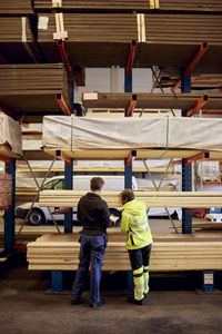 Rear view of multiracial female colleagues with planks on rack working in lumber industry