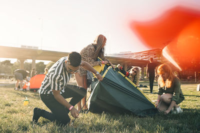 Male and female friends making tent together on lawn during summer
