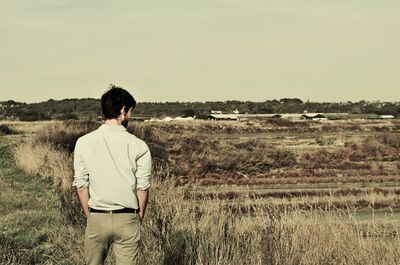 Rear view of man standing on field against sky