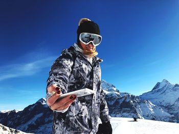 Young man standing on snow covered mountain against blue sky