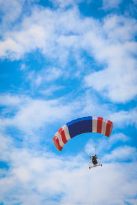 Low angle view of people paragliding against sky