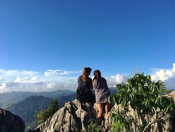 Rear view of friends standing on mountain against blue sky