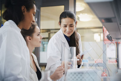 Smiling mature teacher with young female students learning chemistry at laboratory