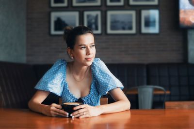 Portrait of young woman holding coffee cup while sitting on table