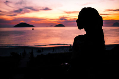 Silhouette young woman standing at beach against sky during sunset