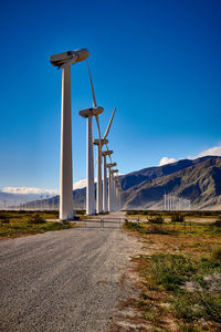 Wind turbines on field by road against sky