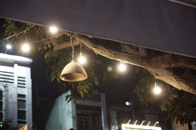 Low angle view of illuminated pendant light hanging on building at night
