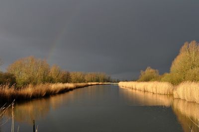 Rainbow over river against cloudy sky