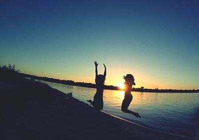 Friends standing on lake against clear sky during sunset