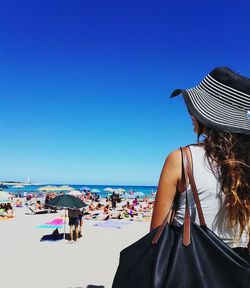 Woman in hat standing at beach against clear blue sky during sunny day