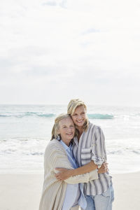 Senior woman and her adult daughter standing on the beach, embracing
