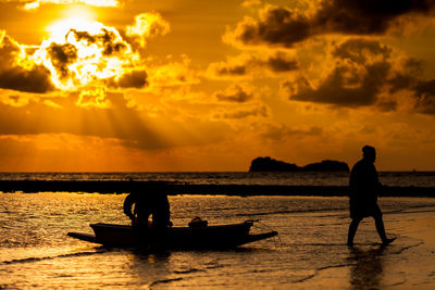 Silhouette people on sea against sky during sunset