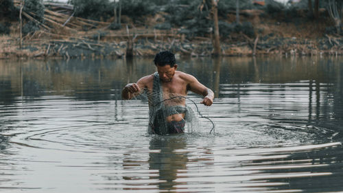 Shirtless man fishing in lake