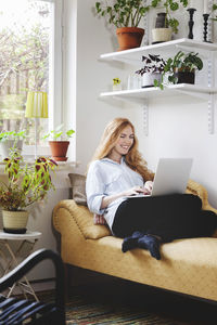 Smiling woman using laptop while resting on chaise longue at home